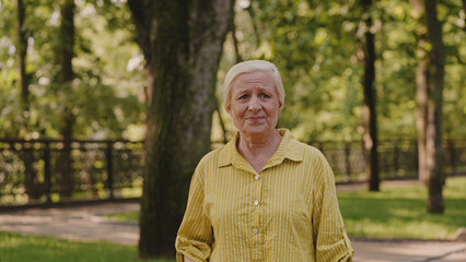 Aged woman standing alone in park, happy with recovery, breathing fresh air