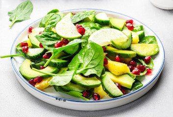 Fresh salad with pineapple, spinach, avocado and pomegranate on gray kitchen table, top view. Healthy vegan eating, clean food, diet, weight loss dish