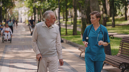 Female doctor talking to senior male patient with disability in park, recovery