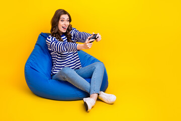 Full size portrait of positive cheerful girl sit comfort bag hold controller play video games isolated on yellow color background © deagreez