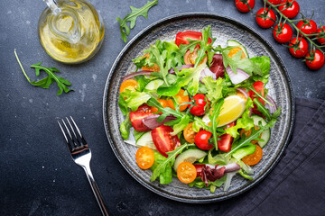 Fresh spring vegan vegetables salad with colorful cherry tomatoes, cucumber, red onion, lettuce, radicchio and arugula. Dark table background, top view