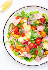 Fish tuna and fresh vegetables salad with cherry tomatoes, red onion, eggs, corn, paprika, lettuce, radicchio and arugula. White table background, top view