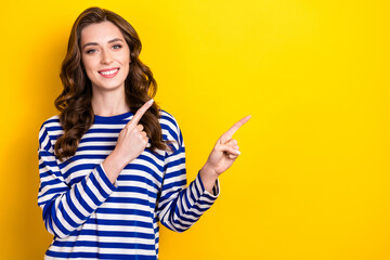 Photo of shiny dreamy young girl dressed striped pullover pointing two fingers empty space isolated yellow color background