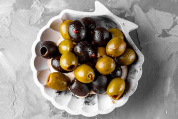 Delicious black and green olives in plate on gray background