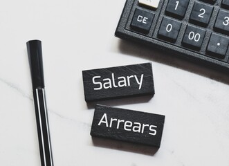 Salary arrears inscription on painted wooden chips with calculator on desk. Top view. 