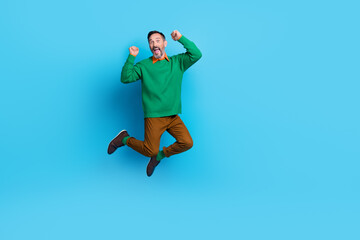 Fototapeta na wymiar Full body photo of mature handsome man jumping high energetic raise fists dressed stylish green outfit isolated on blue color background