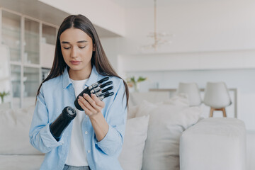 Disabled young woman getting used to new bionic prosthesis. Girl setting her robotic hand functions.