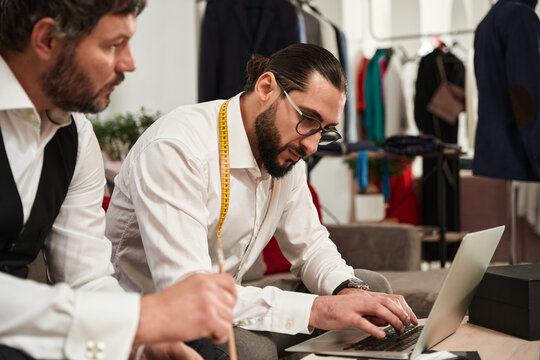 Two modern clothiers using laptop in atelier