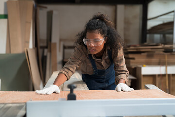 African American female carpenter worker working with saw machine at wood processing plant. Female...