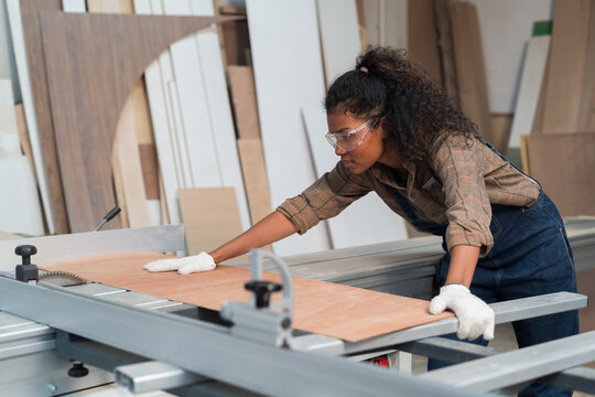 African American Female Carpenter Worker Working With Saw Machine At Wood Processing Plant. Female Joiner Worker In Safety Uniform And Equipment Tools Working In Wood Factory. Manufacturer Industry M
