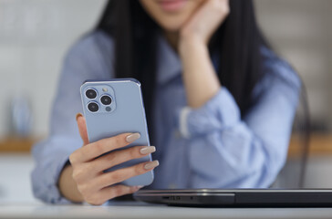 Young asian girl holds blue smartphone with triple camera in hand. BIPOC female from Vietnam using modern mobile phone app