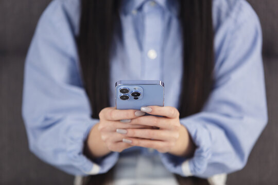Girl typing sms message on blue mobile phone with triple camera. Close up photo of young female communicating online with modern smartphone