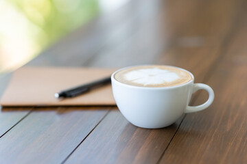 Hot latte coffee in white cup on wooden table, blurred background in cafe
