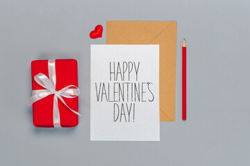 Falt lay composition of craft paper envelope and white card with hand written St. Valentines day...