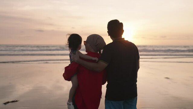 Happy Modern Muslim Southeast Asian Indonesian Family Enjoying Sunset Together on The Beach. Silhouette of Father Mother and Child in Slow Motion.