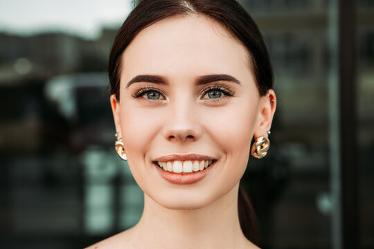 Pretty brunette caucasian woman standing outside street with white teeth beaming healthy smiling lady. Happy millennial girl model posing looking at the camera, head shot portrait.

