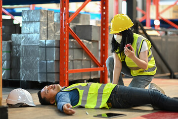 Warehouse worker lying unconscious on floor after accident while colleague calling for help or reporting work accident by walkie talkie