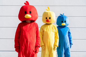 Friends wearing multi colored duck costumes standing in front of white wall