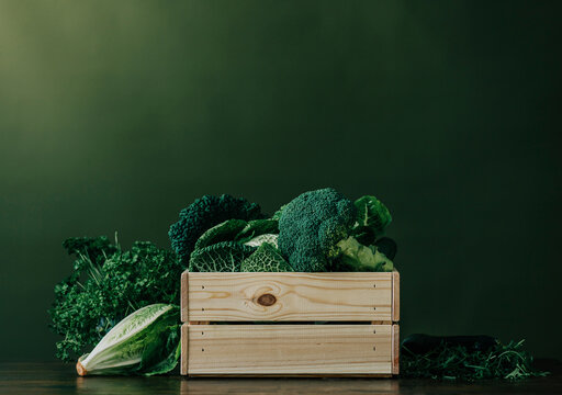 Crate full of fresh raw vegetables in front of green wall