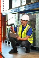 Warehouse worker using digital tablet, checking quantity of storage product in aisle between shelves full of packed boxes