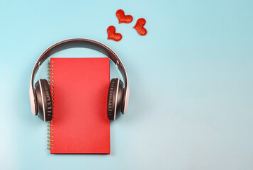 flat lay of red notebook covered with headphones on blue background decorated with red glitter hearts , copy space. Audio book, podcast, .love diary, valentine's day.
