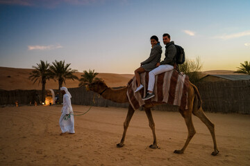 Couple riding a camel during Dubai desert safari at the safari camp, Dubai United Arab Emirates © Fokke Baarssen