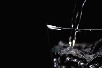 Water is pouring into transparent glass with black background to encourage drink or saving water.
