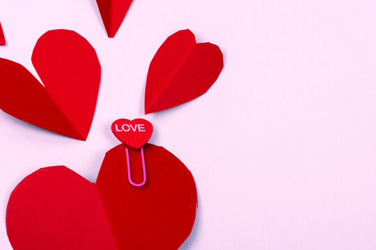 Valentine's day background. Close-up of red hearts on pink background. Paper clip with heart shape and the word "love" written on it.