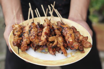 Hands holding a plate of satay. Pork Satay or Sate Babi served on a plate. Selective focus.