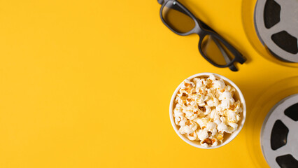 Top view popcorn cup, 3d glasses, film reels on yellow background banner with copy space. Leisure and entertainment concept