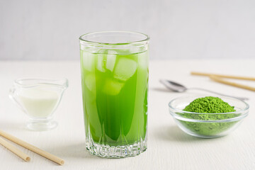 Organic homemade healthy matcha latte made of green tea leaves ground powder mixed with milk or water served in glass on white wooden table with paper straw for breakfast contains caffeine and tannin