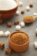 White and brown sugar in bowl on grey background. Vertical photo