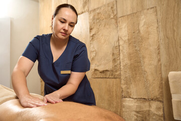 Masseuse kneads the client back muscles with stroking movements