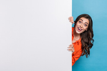 Photo portrait of young pretty girl hiding behind white wall excited dressed stylish orange outfit isolated on blue color background