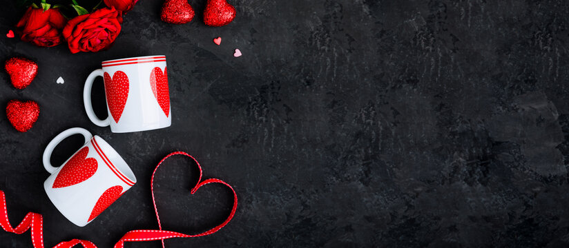 Valentine's Day table setting with two cups, red ribbon and hearts on dark background