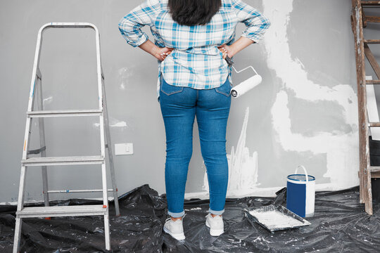 Cropped shot of woman standing with hands on hips preparing to paint wall