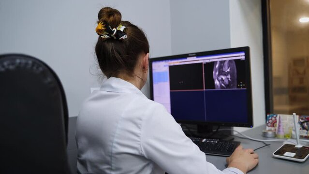 Female lab technician sitting back to camera facing the computer screen. Expert analyzing the MRI scans of a patient.