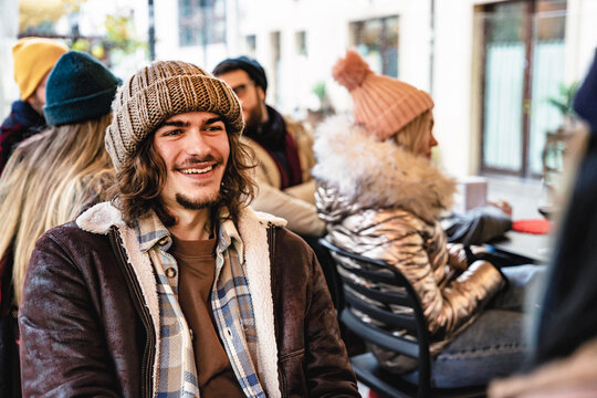 Young trendy hipster guy wearing winter clothing having fun at pub -Happy group of friends sitting outdoors at restaurant enjoying together free time-Youth culture-Friendship and lifestyle concept 