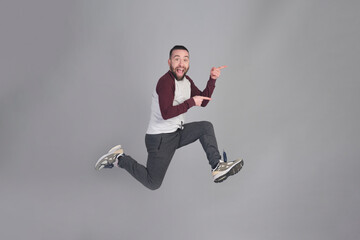 Young man pointing to copy space in studio shot while jumping