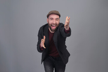 Young man in jacket and cap enthusiastic with arms forward in a studio shot - 565303056