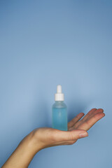 Female hands with serum in bottles on blue background