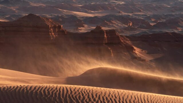 Sand blowing over dunes in wind, red cliffs on background, Gobi desert. Mongolia