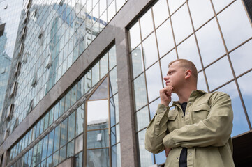 A pensive man stands against the backdrop of a skyscraper.