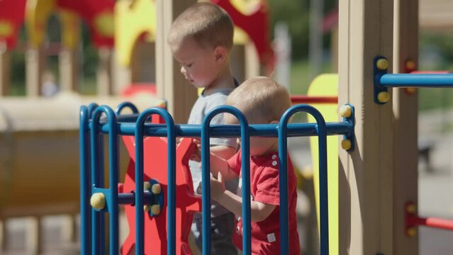 two sibling brothers playing together captain boat wheel on colorful children playground sunny summer day. two little boys spinning steering wheel on toy ship outdoors in hot daytime. 
