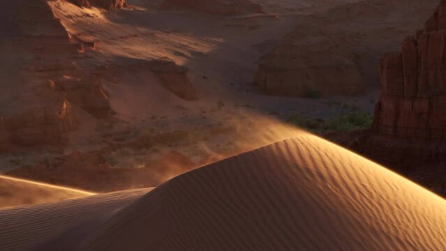 Sand blowing over dune in wind in red canyon, Gobi desert. Mongolia