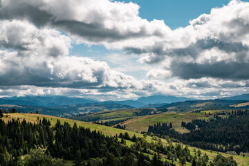 Fototapeta na wymiar Beautiful mountain landscape panorama view with coniferous forest on a mountain range with forested hillsides, meadows covered with grass, clouds in the blue sky on a sunny day. Ecotourism