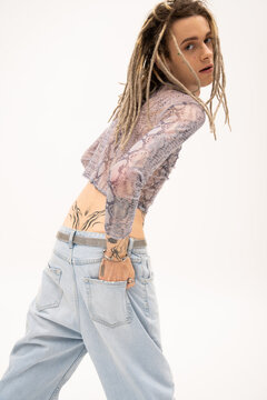 Young queer person with dreadlocks and tattoo posing isolated on white.
