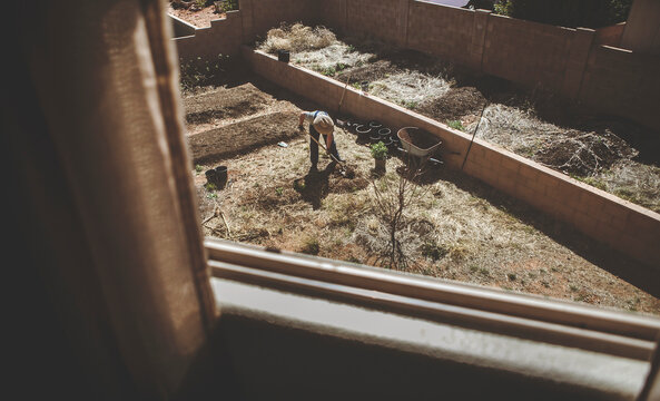 High angle view of man digging soil in backyard seen through window