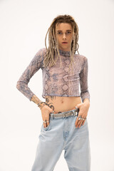 Tattooed nonbinary person in crop top touching jeans isolated on white.