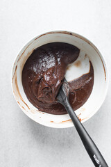 Thick chocolate madeleine batter that has rested in a white bowl, thick chocolate cake batter, brownie batter in a bowl